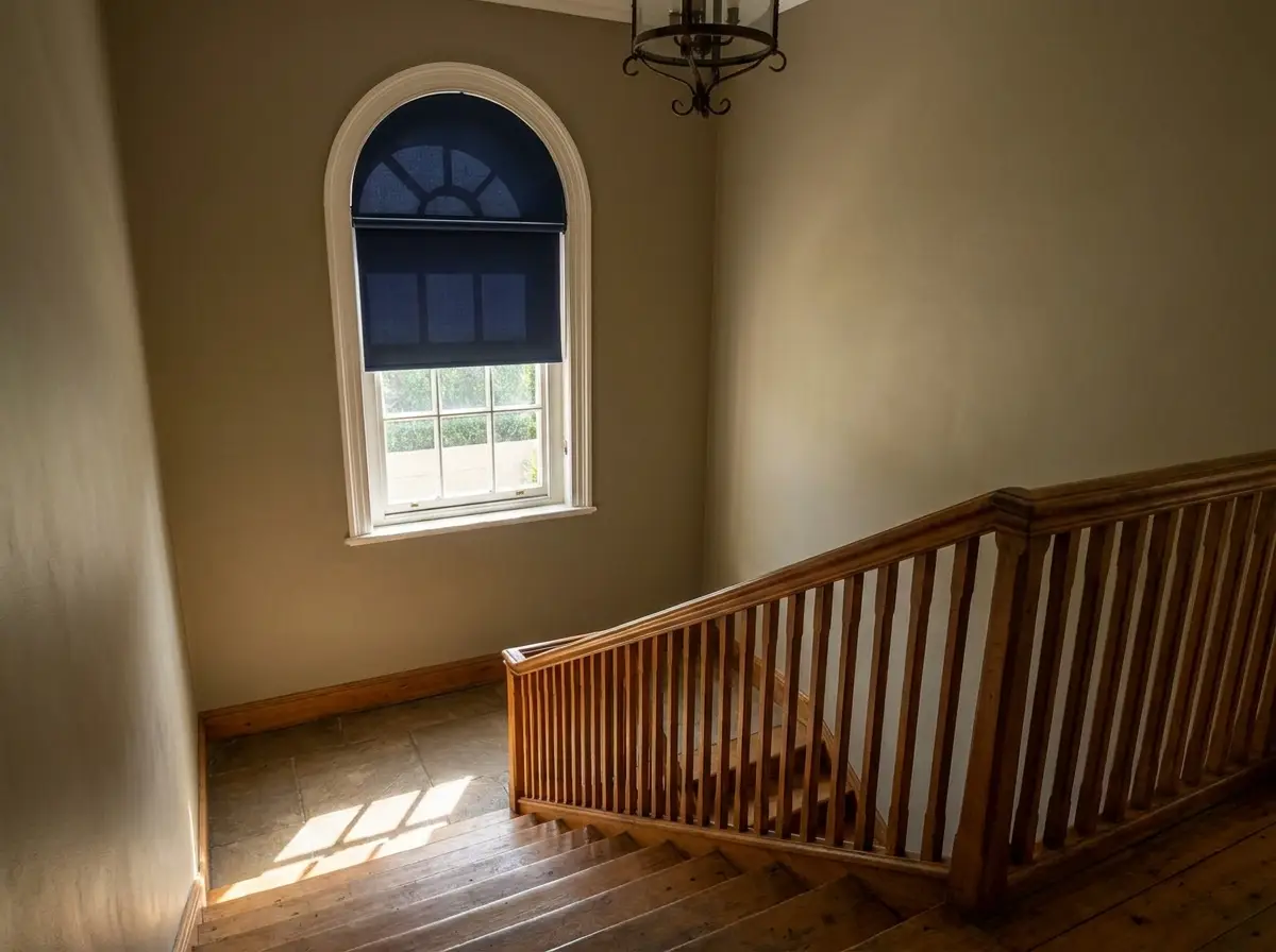 Motorised navy roller blind high on an arched stairwell window in a Saxonwold home